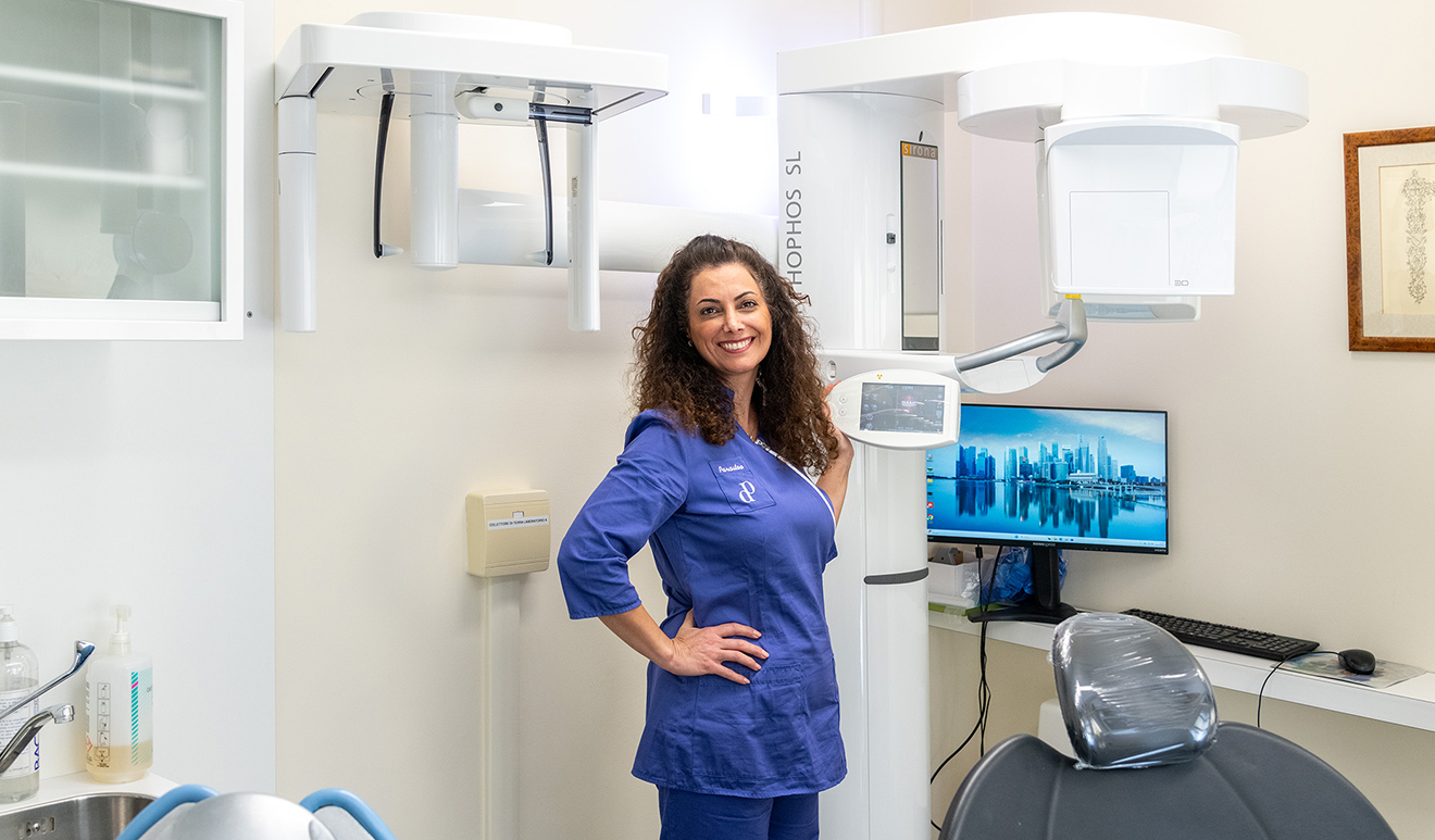 Dentista sorridente nel suo studio a Bolzano, accanto a un dispositivo Sirona Orthophos SL Cone Beam CT per radiografie dentali digitali