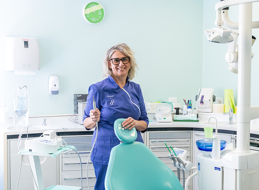 La dottoressa Carmen Pellitteri sorride in uniforme blu con uno strumento chirurgico piezoelettrico nello studio dentistico a Bolzano