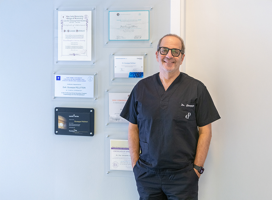 Il Dr. Giuseppe Pellitteri sorride davanti a una parete con i suoi attestati e certificazioni professionali