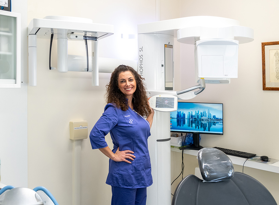 Una dottoressa sorridente in uniforme blu posa accanto a un Cone Beam CT all'avanguardia presso lo Studio Odontoiatrico Pellitteri a Bolzano