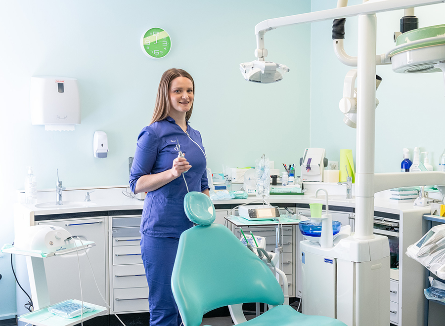 Una dentista in uniforme blu, con uno strumento in mano, in uno studio dentistico moderno e ben attrezzato per la prima visita